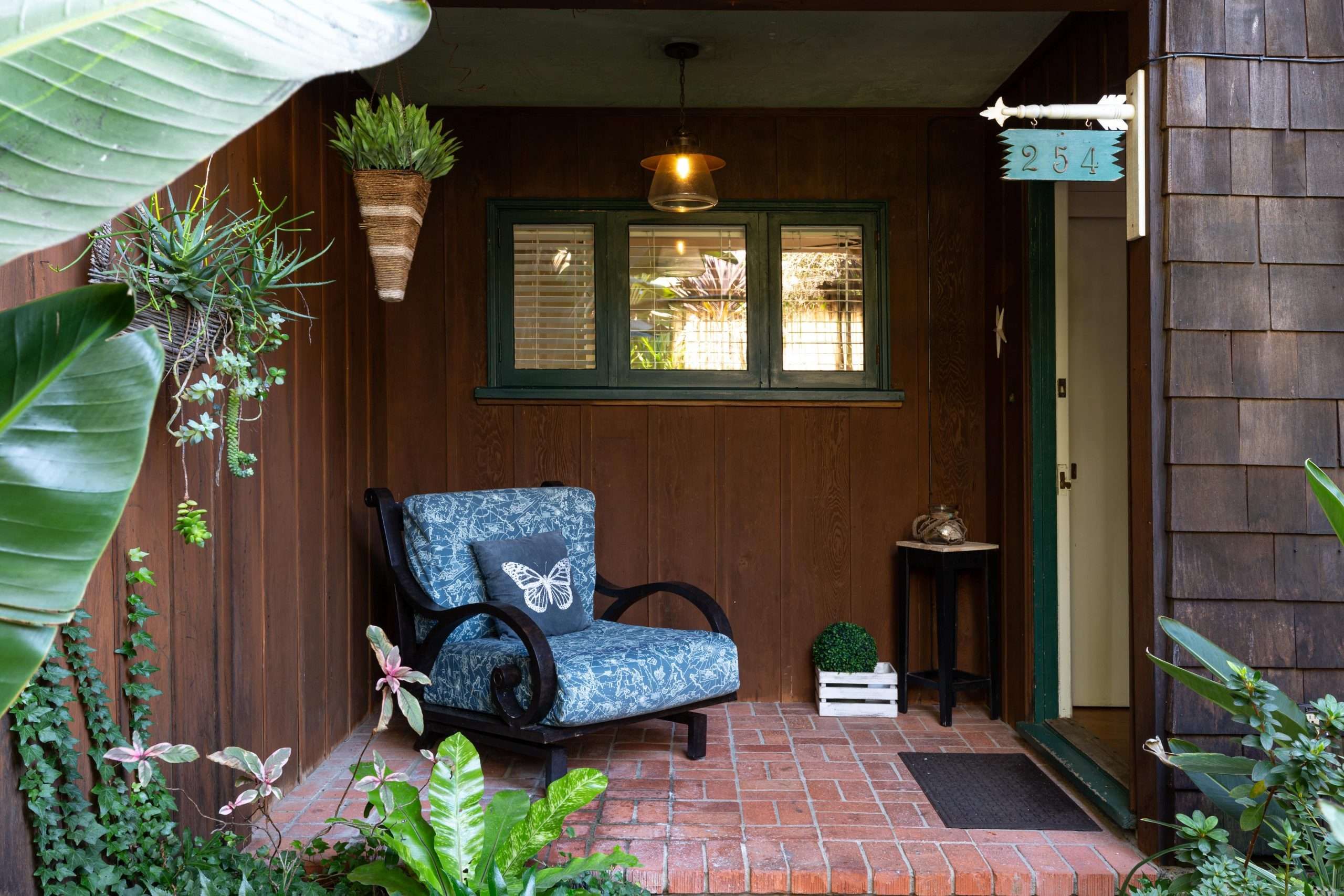 Covered front porch with a blue patterned armchair, brick floor, and the cottage's 254 house sign