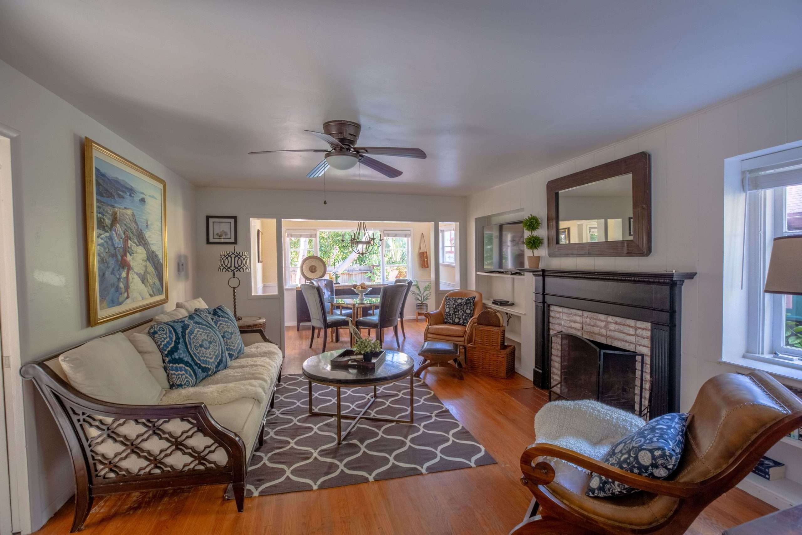Living room with a cream sofa, patterned rug, and brick fireplace, opening onto the dining area