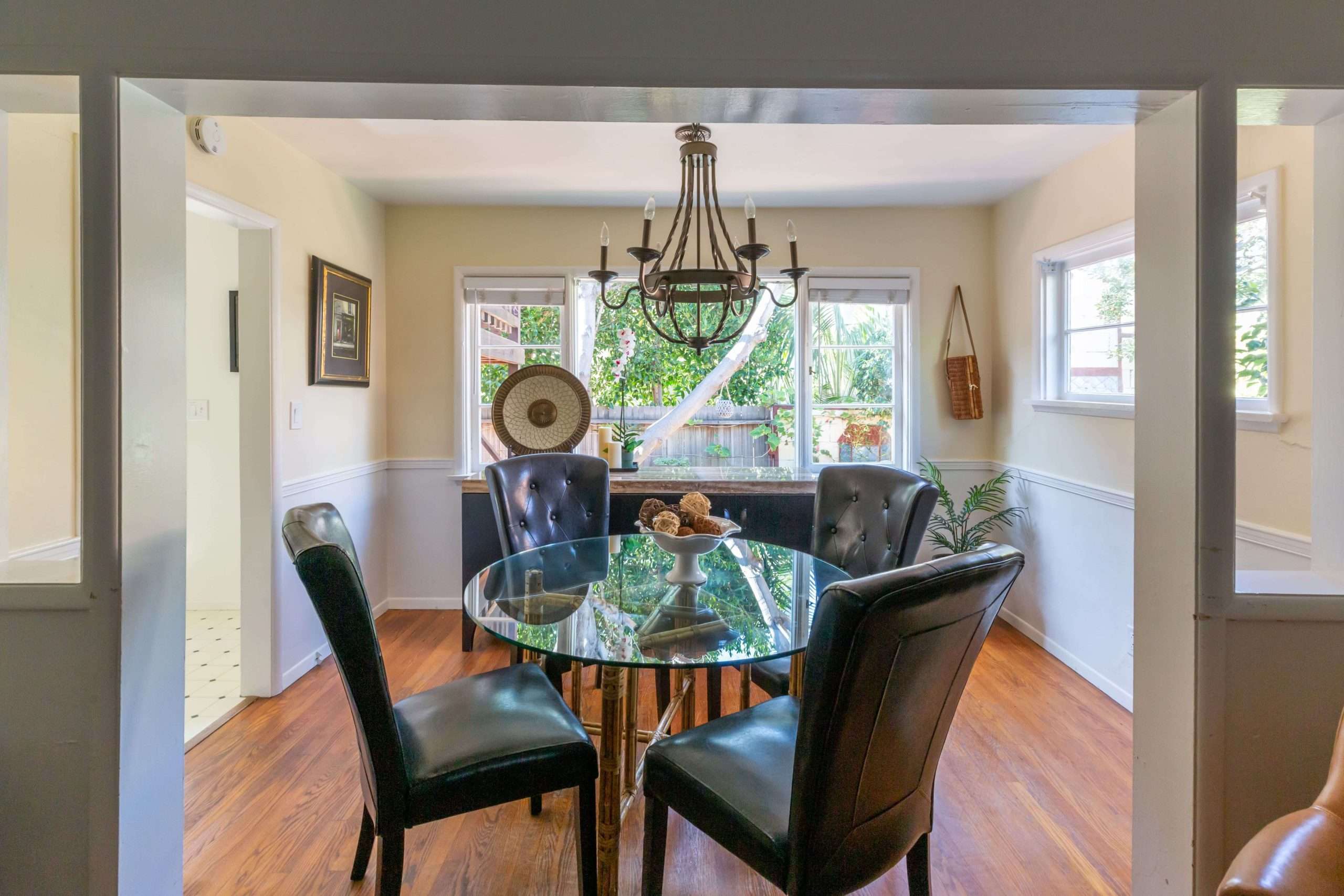 Dining area with a round glass table, four dark leather chairs, and a wrought-iron chandelier