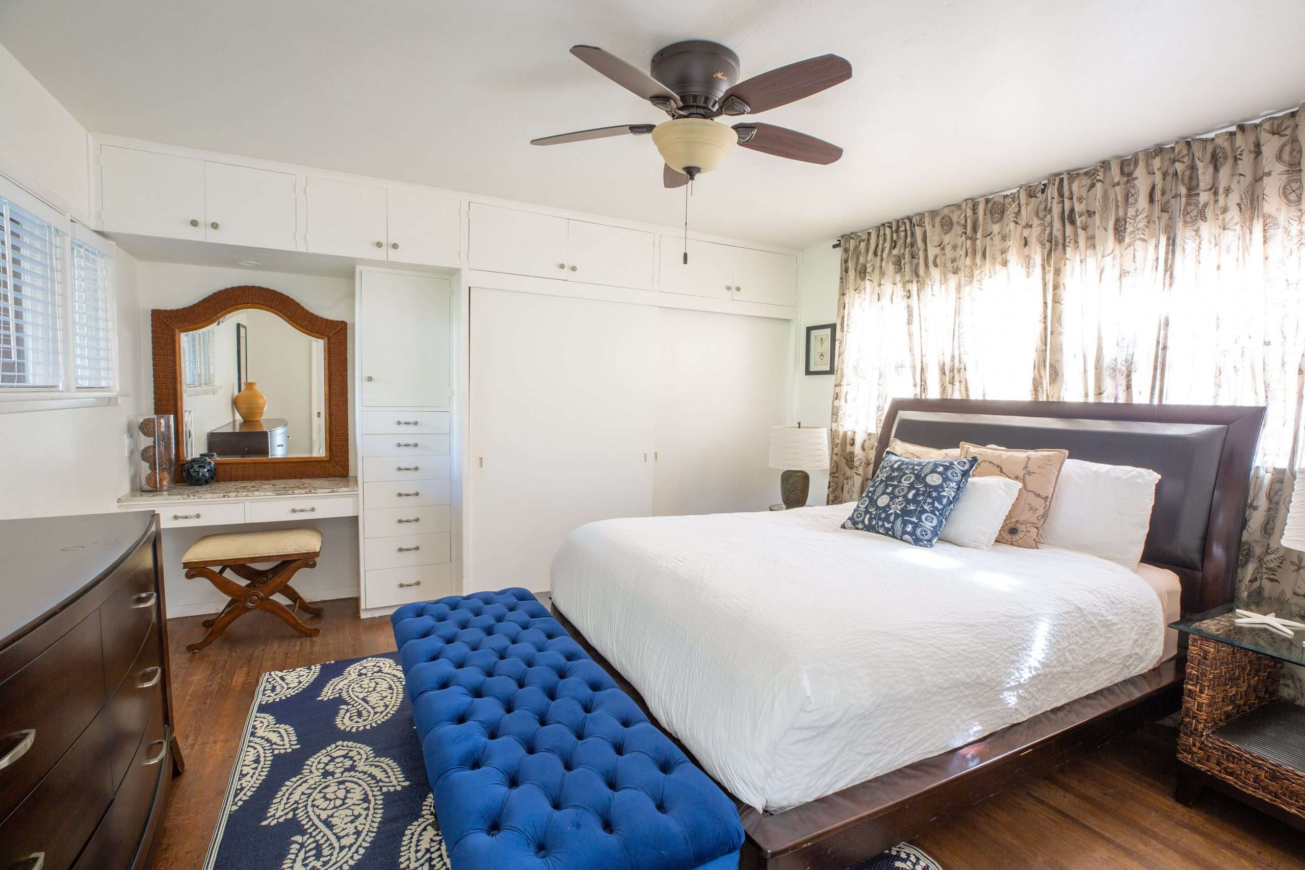 Bedroom with a queen bed, blue tufted bench, built-in vanity mirror, and ceiling fan