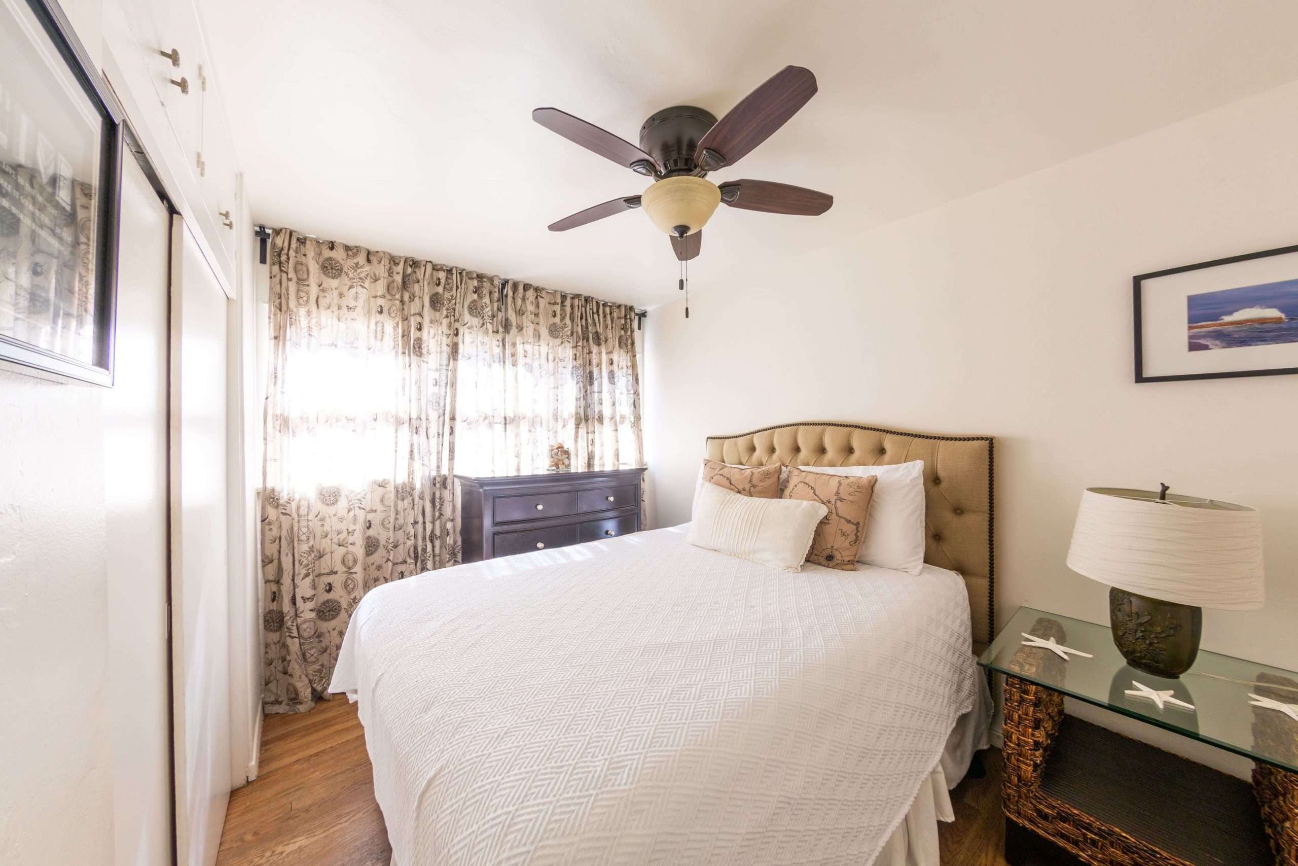 Second bedroom with a queen bed, tufted headboard, and patterned curtains